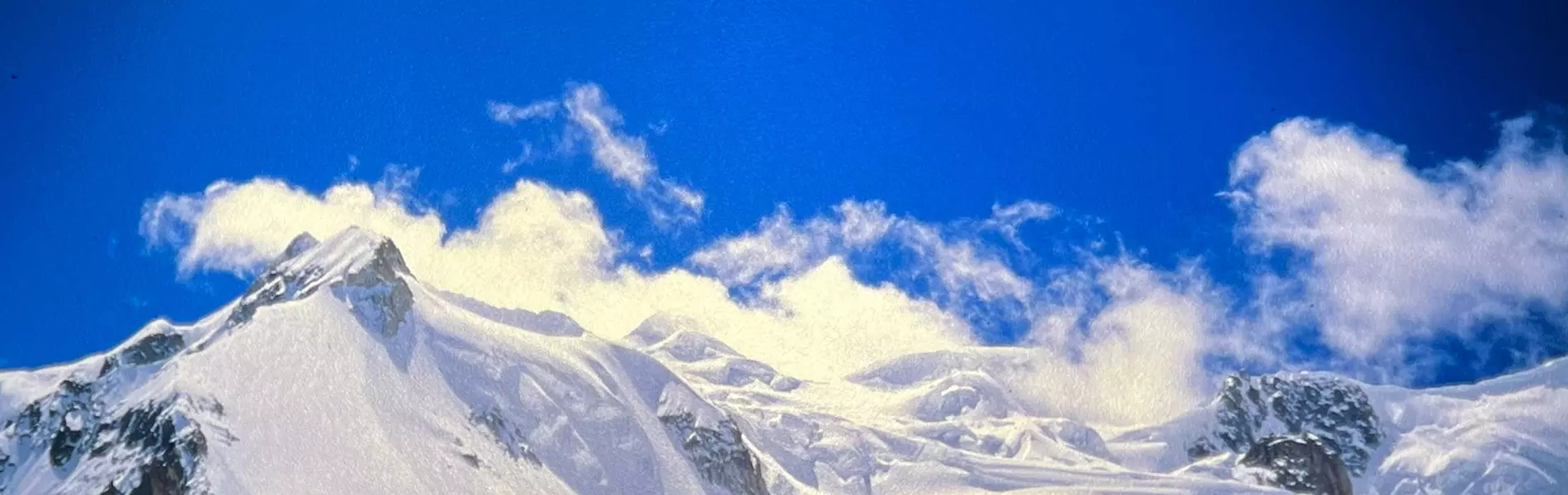 Drie klimmers in kleurrijke jassen, met zonnebrillen op en uitgerust met klimuitrusting, staan met hun rugzakken op een besneeuwde berg, omringd door met sneeuw bedekte bergtoppen en een stralend blau